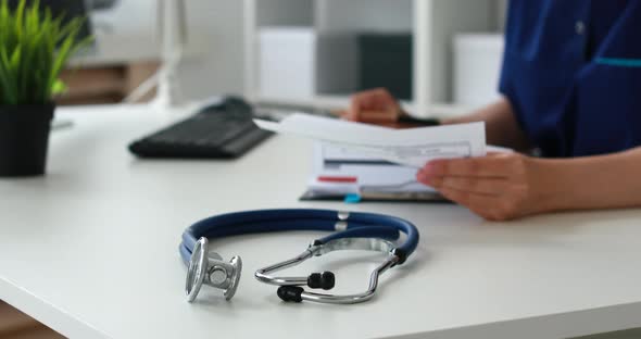 Blue Stethoscope on Table in Focus in Foreground, Rear Doctor Filling Papers