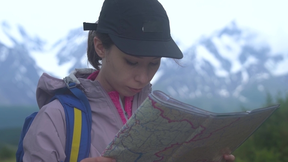 Hipster Young Girl with Backpack on Peak of Mountain Looking Map. Tourist Traveler on Background