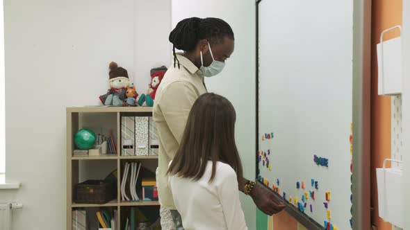 Children in Protective Masks Learn English By Composing Words on a Magnetic Board During a Pandemic alt