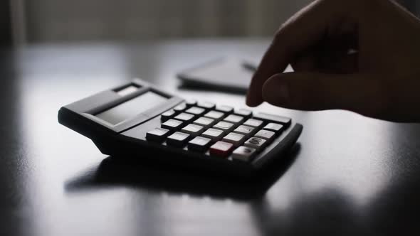 Hand of a Businessman Using a Calculator and Taking Notes in Notepad
