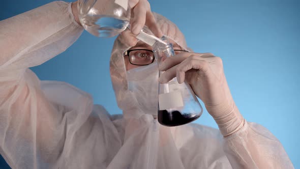 Man in Protective Suit Medical Mask Gloves Holds Mixes Liquid in Flasks
