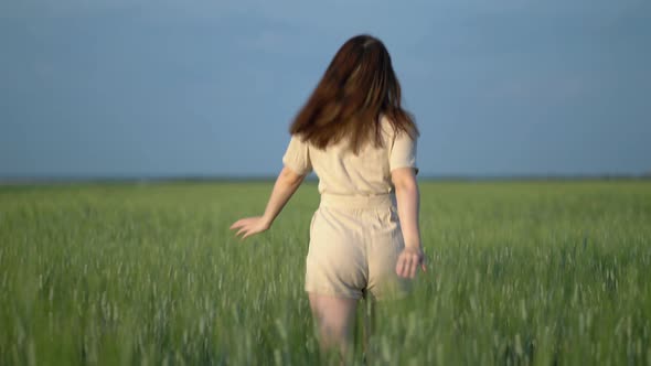 A Beautiful Girl in a Beige Suit Runs Through a Wheat Rye Oats Field alt