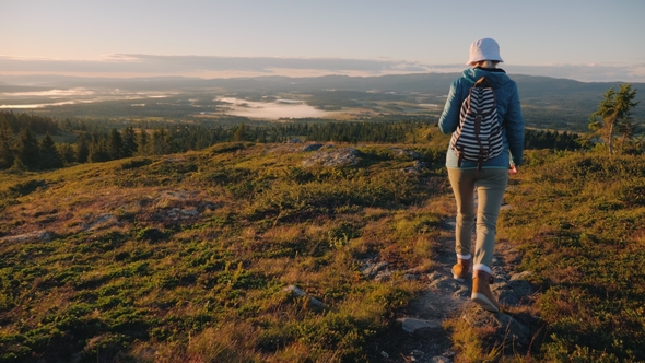 A Woman Traveler with a Backpack Behind Her Back Walks Through the Picturesque Highlands in Norway alt