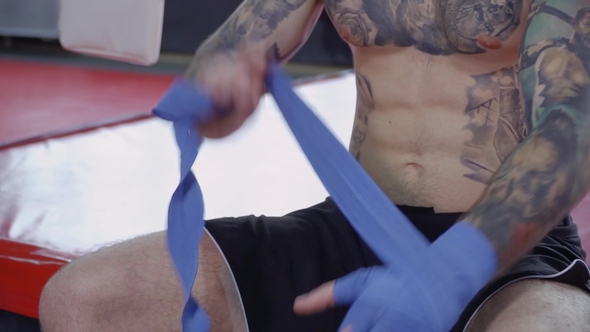 Boxer with Tattoos and in Boxing Shorts Bandages His Hand alt