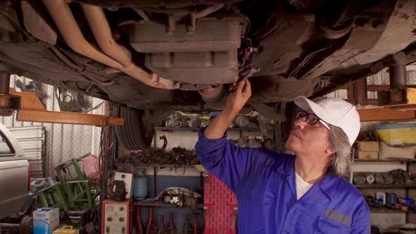 Male Auto Mechanic Inspects the Car Undercarriage Way in Garage alt