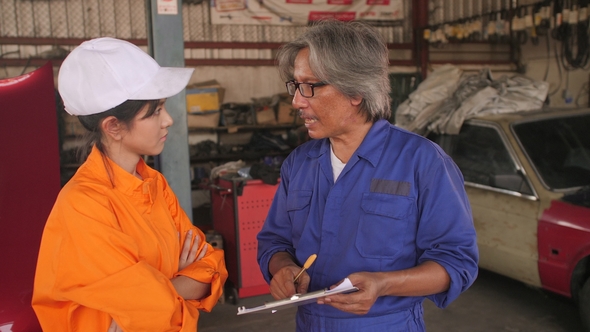 Mechanics Discussing Over Clipboard in a Car Workshop.