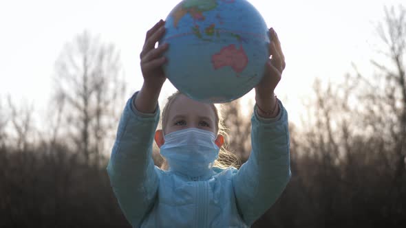 Sad Child Girl in Medical Mask Holding the Globe. alt