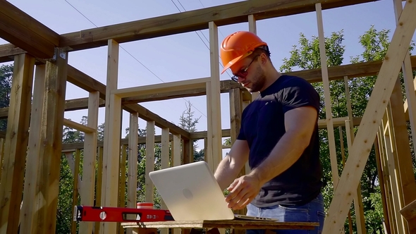 Builder Is Looking on a Screen of Laptop on a Construction Site of House, Taking Building Level and alt