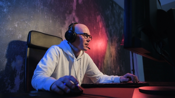 Young Pro Gamer Playing in Online Video Game, Talks with Team Players Through Microphone. Neon alt
