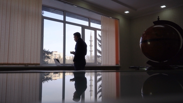 Businessman Standing Near a Window and Drinking Coffee