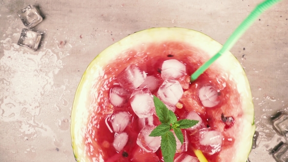 Alf of Watermelon with Ice, Mint and Slices of Watermelon and a Straw Revolves Around on the Table