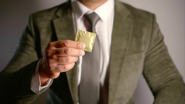 Agent Holding a Single Condom in a Golden Package and Putting It in Inner Pocket of a Jacket alt