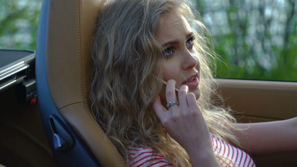 Young Pretty Blonde Woman Talking on Her Phone in Her Brand-new Car with Modern Inside and Leather alt