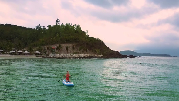 Girl Swims Sitting on Paddleboard Turning From Beach To Ocean alt