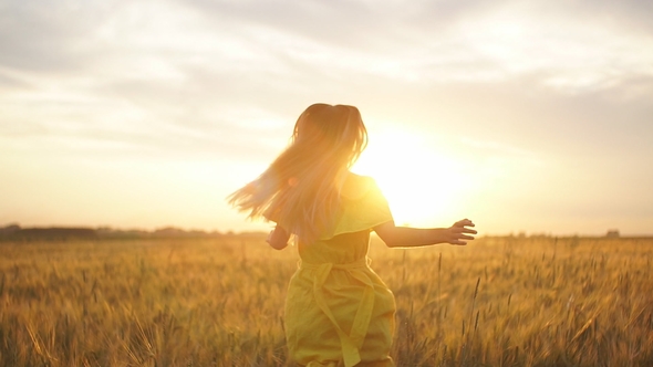 A Girl in a Red Dress Runs Across the Field at Sunset