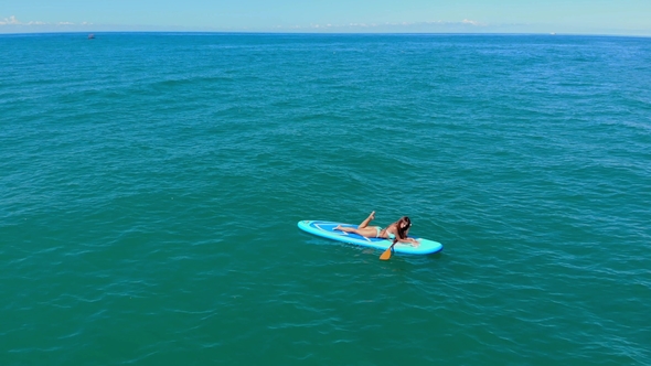 Drone Shot of Top View on Young Female Lies in a Paddle Surf Board Known As Sup Surfing in Turquoise