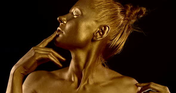 Portrait in Profile of a Girl with Golden Skin. She Closes Her Eyes, Runs Her Finger Over Her alt