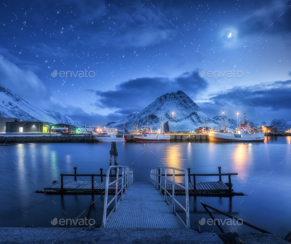 Fishing boats near pier on the sea and snowy mountains at night - Stock Photo - Images