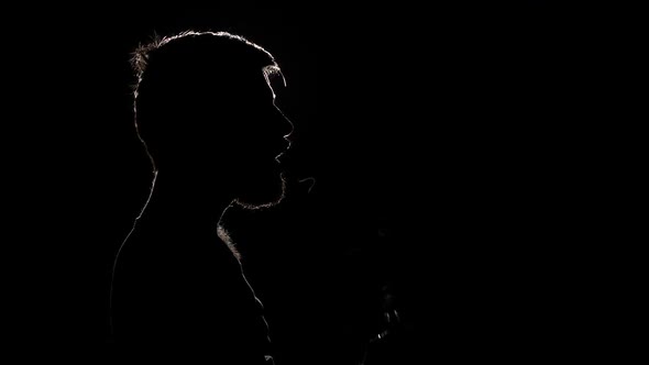 Brutal Sad Man Sits and Smokes an Electronic Cigarette. Black. Silhouette. Slow Motion alt