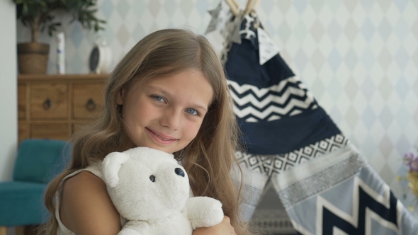 Sweet Girl Is Hugging a Teddy Bear, Looking at Camera and Smiling