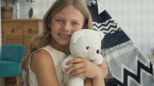 Cute Little Girl Is Hugging a Teddy Bear, Looking at Camera and Smiling