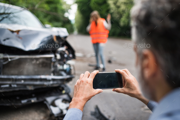 Unrecognizable man taking pictures of a broken car after an accident. - Stock Photo - Images