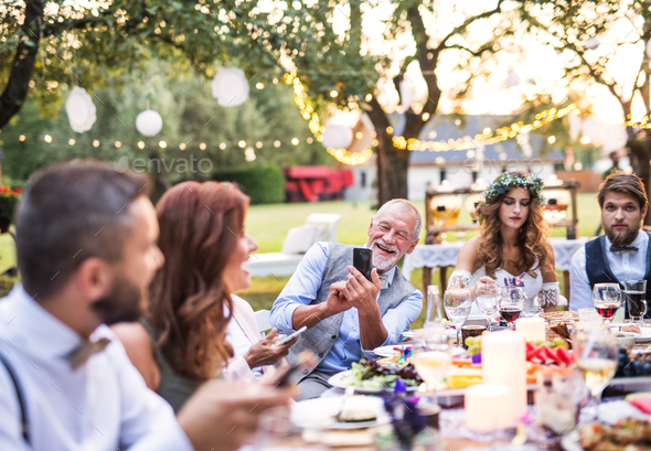 A senior man taking selfie at the wedding reception outside in the backyard. Stock Photo by halfpoint