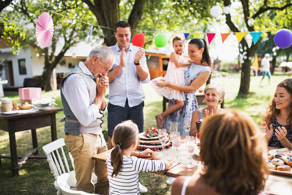 A senior man with an extended family looking at the birthday cake, crying. Stock Photo by halfpoint