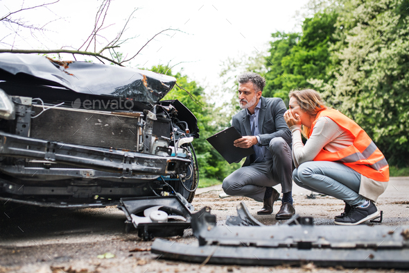 An insurance agent and a woman driver looking at the car on the road after an accident. - Stock Photo - Images