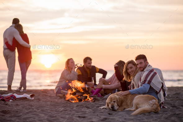 Couple enjoying with friends at sunset on the beach Stock Photo by dotshock