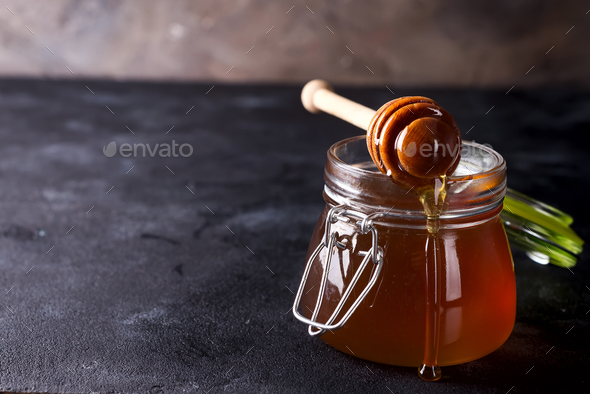 Honey dripping from a dipper into the jar full of fresh honey on dark stone background Stock Photo by lyulkamazur