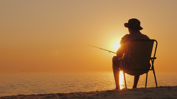 A Young Man Is Sitting on the Seashore, Fishing. Relaxing in the Open Air alt