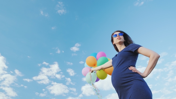Happy Pregnant Woman Playing with Balloons Against the Blue Sky alt