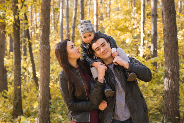 Family walking in autumn park. Daughter sitting on dad\'s shoulders. Stock Photo by Satura_