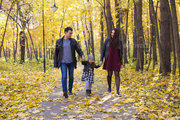 people, family and leisure concept - family with a young daughter walking in autumn park Stock Photo by Satura_