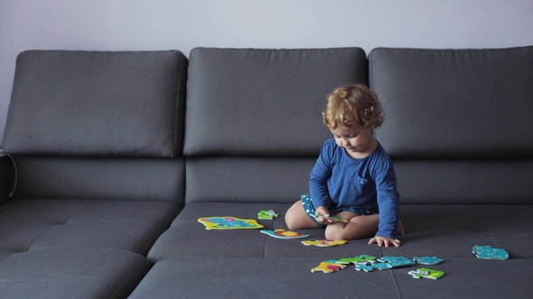 Little Girl with Curly Blond Hair Plays with Puzzle Toys . Blue Clothes. Feels Happy