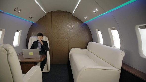 Young Confident Lawyer Businessman Is Working with Laptop Sitting in Entrepreneur Airplane Interior alt