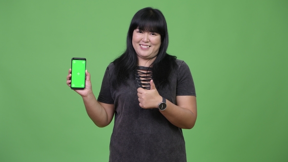 Happy Overweight Asian Woman Showing Phone and Giving Thumbs Up alt