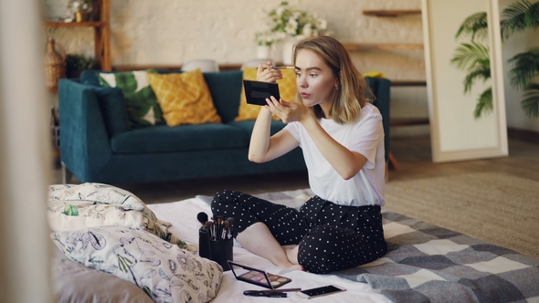 Beautiful Blond Girl Is Putting on Makeup Painting Eyebrows with Brush and Cosmetics Kit Sitting on alt