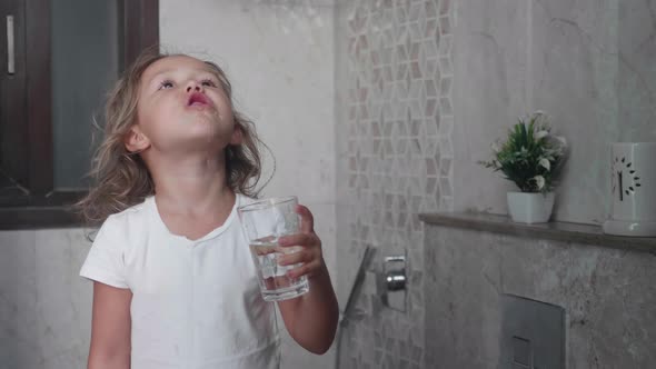 Little curly child girl rinses her mouth with water.