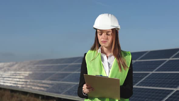 A Female Engineer is Conducting an Inspection of Solar Panels and Recording the Data in Documents alt