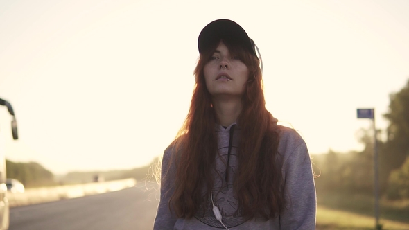 Portrait of a Girl Hipsters at Sunset. Red-haired Girl Wearing Headphones and a Cap