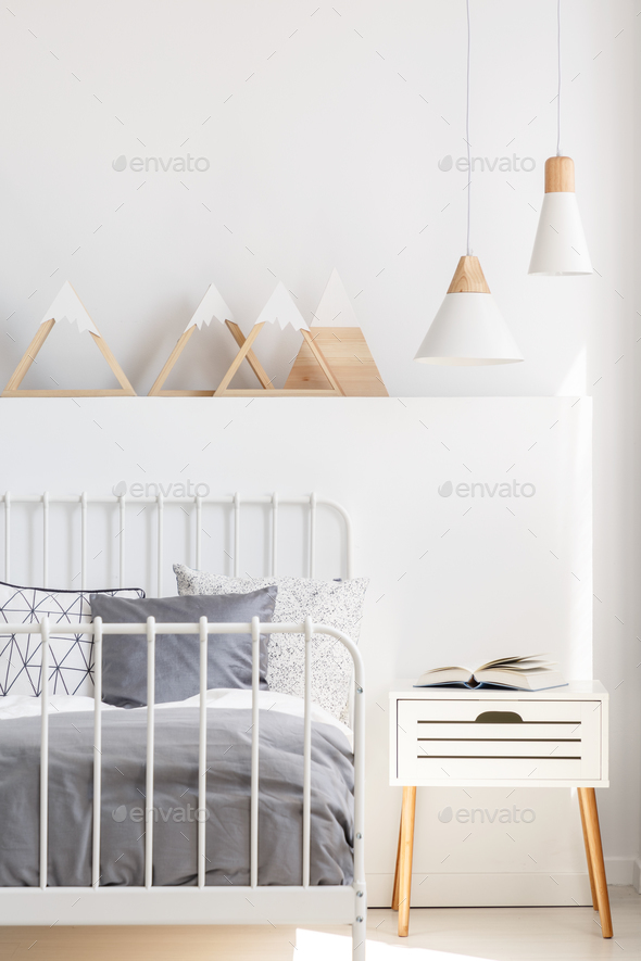 Lamps above bedside cabinet next to bed in white child\'s bedroom