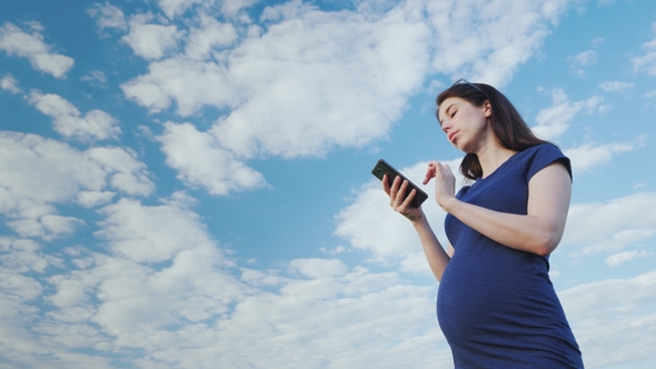 Pregnant Woman Taking a Picture Against the Blue Sky alt