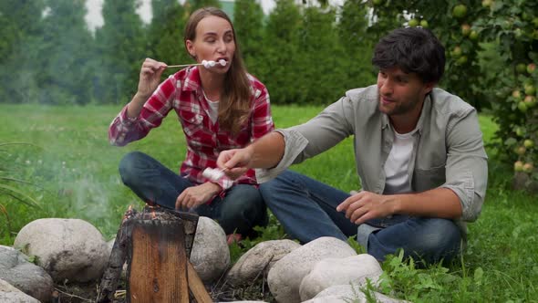 Young Couple Roasts Marshmallows on a Picnic By the Campfire alt