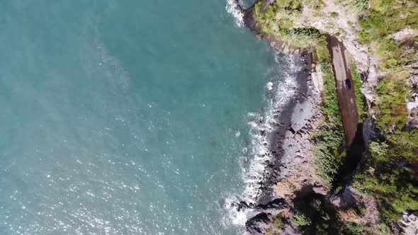 Aerial view of the ocean and cliffs. A car appears from the tunnel.