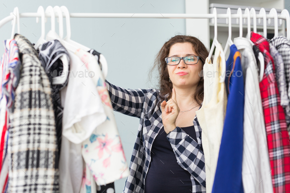 People, clothing and style concept - portrait of a pretty woman looking through the wardrobe Stock Photo by Satura_