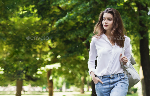 Casual woman walking alone through green park Stock Photo by Prostock-studio