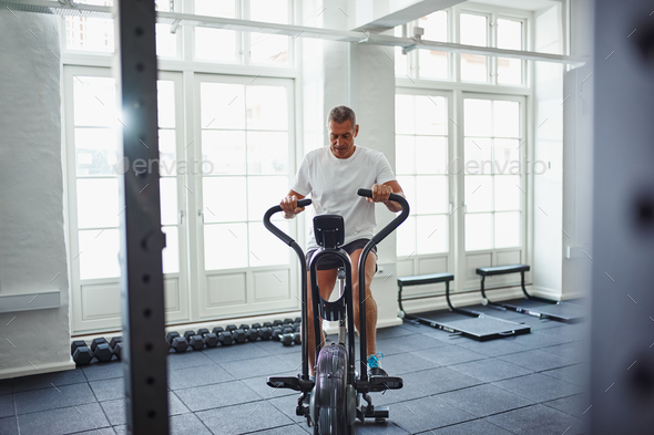 Fit mature man in sportswear exercising on a stationary bike Stock Photo by UberImages