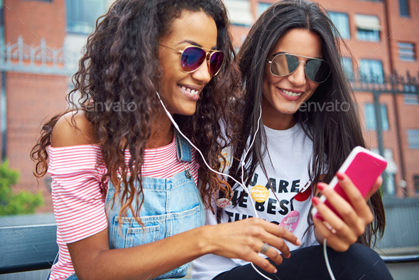 Young girlfriends sitting together outside streaming video on a smartphone - Stock Photo - Images